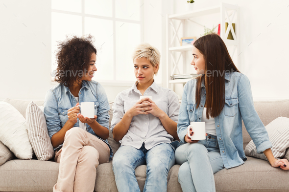Three young female friends with coffee chatting at home - Stock Photo - Images