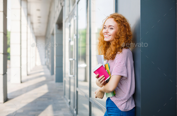 Young smiling redhead student girl with cup of coffee and books - Stock Photo - Images