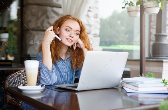 Young serious redhead girl looking at laptop sitting outdoors - Stock Photo - Images