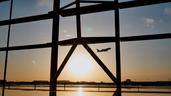 Silhouette of an Airplane Taking Off at Sunset at Beijing Airport in the Background of a Window. alt