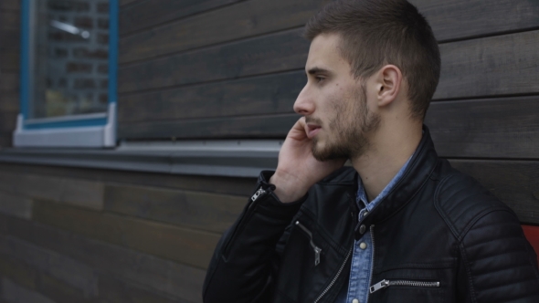 Stylish Man Speaking at Smartphone at Wooden Building alt