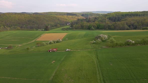 drone footage of a tractor driving away from a huge green meadow after spraying with its sprinkler s alt