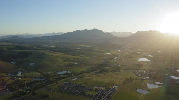 Sun rays sunrise over homes in vineyards farmland with ponds, Stellenbosch, Aerial Drone alt
