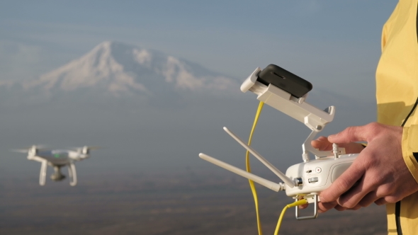 Man Hands Control Flying Drone Near Mountain