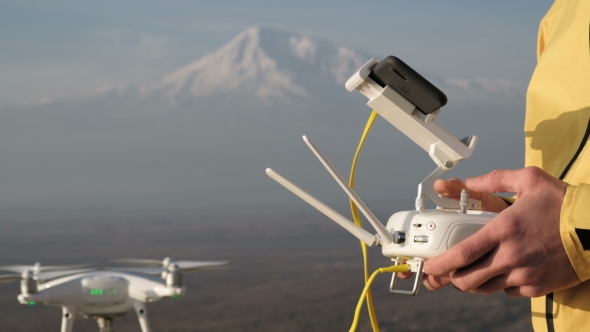 Man Hands Control Flying Quadcopter near Mountain alt