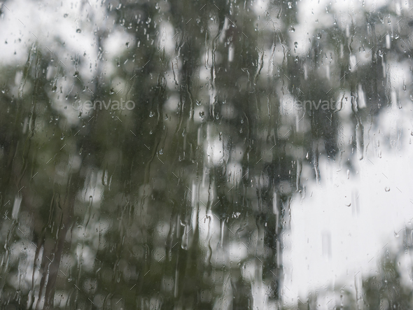 Rain drops on window glasses surface with trees against the sky - Stock Photo - Images