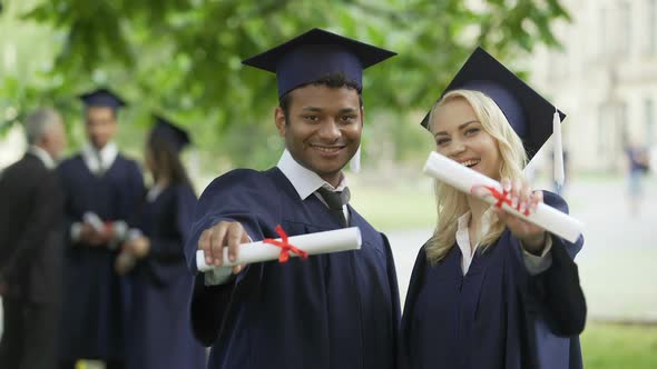 Male and female graduates showing diplomas and smiling, complete high education alt