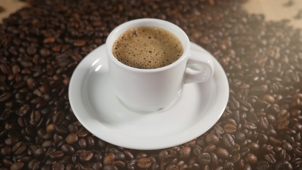 Coffee Cup and Coffee Beans A White Cup of Evaporating Coffee Foam on a Table with Fried Beans.