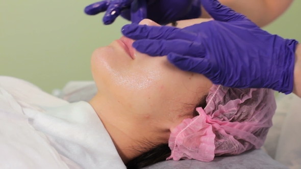Cosmetologist Applies Cream on Face of Lying Woman Girl in Bonnet Lying on the Session at the