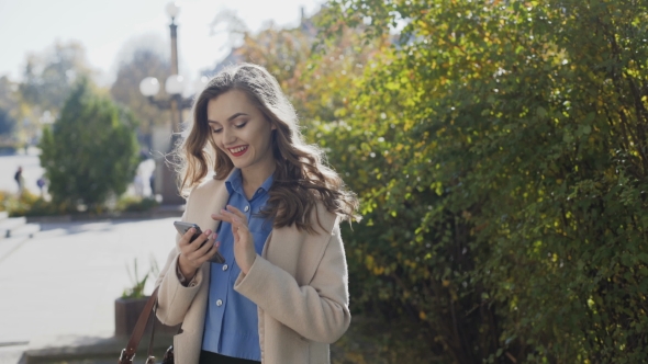 Beautiful Girl in a White Coat Uses a Smartphone and Smiling alt