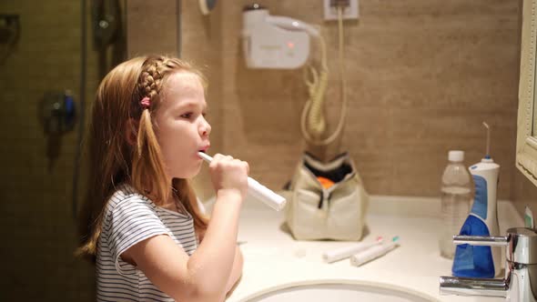 Girl Brushes Teeth in Bathroom with an Electric Toothbrush alt