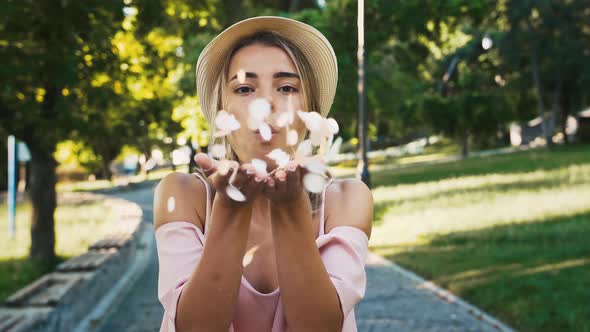 Young Girl in Hat and Pink Dress is Blowing Off Confetti From Her Palms and Smiling alt