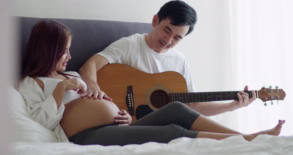 Asian husband and pregnant wife spend time together in the bedroom.