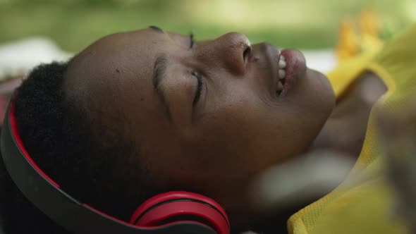 Side View Headshot of Smiling African American Woman in Headphones Lying in Park Enjoying Music alt