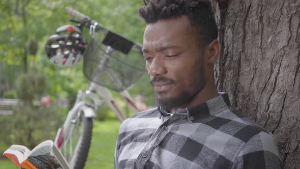Portrait Confidient Cute Handsome African American Man Sitting Near His Bicycle Under an Old Tree in alt