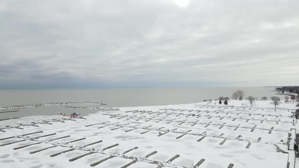 Partially frozen lake with rocky snow covered seawall protecting the empty marina and cloudy day.