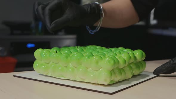 Confectioner's Hands Decorate Green Mousse Cake in the Form of Apples alt