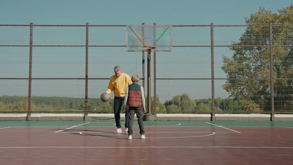 Father Teaches Son How to Outplay in Basketball on a Court on a Sunny Day