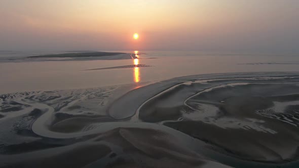 Aerial, rising, drone shot overlooking scenic patterns on a beach, towards sunset alt
