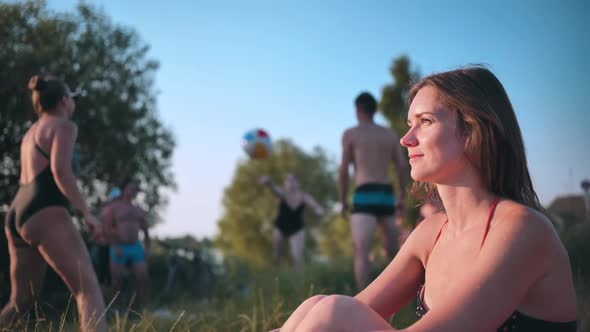 A Girl in a Swimsuit Against the Background of Vacationers and Playing People on the Beach alt