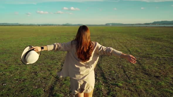 slow-motion of cheerful woman running across the green field with sunlight alt