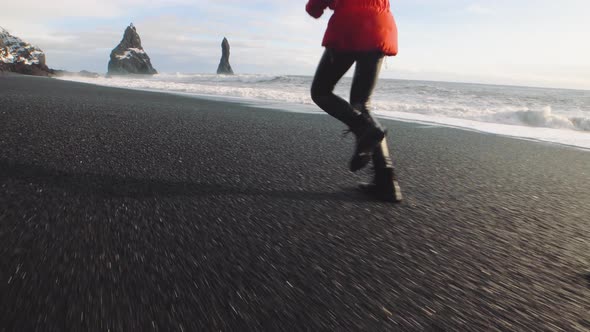 Traveler Woman in a Red Jacket Running on Volcanic Black Sand Beach in Iceland alt