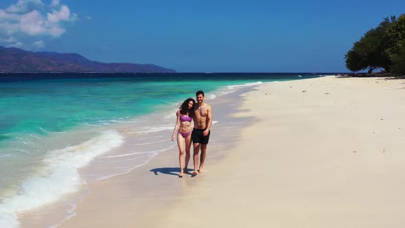 Guy and girl happy together on idyllic island beach vacation by turquoise water with white sandy bac alt