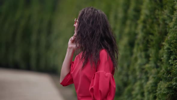 Woman in Red Dress and Sunglasses is Walking in Park and Calling By Mobile alt
