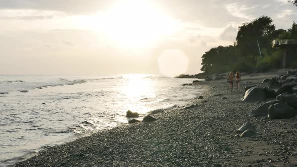 Couple Walks at Beautiful Sunrise on the Volcanic Rocky Seashore in Amed Bali Handheld Ultrawide alt