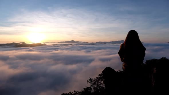 Slow motion of a female traveler sitting on the mountain peak, watching sunrise and sea of fog