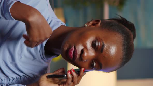 Vertical Video Remote Black Employee Speaking at Phone While Working at Laptop Late alt