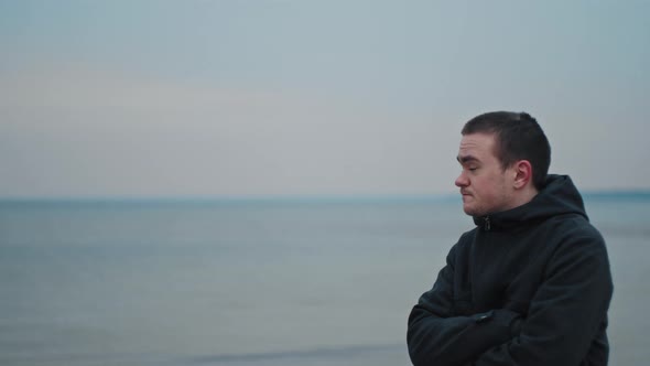 young guy looks into the distance at the sea surface, he is sad and cold