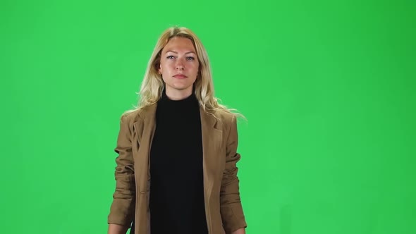 Blonde Girl in a Black Turtleneck and Stylish Brown Jacket Going Against a Green Screen. Slow Motion alt