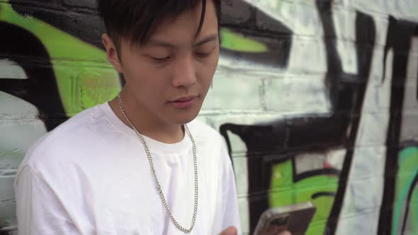 Young Asian Man Looking Into Smartphone Outdoors alt