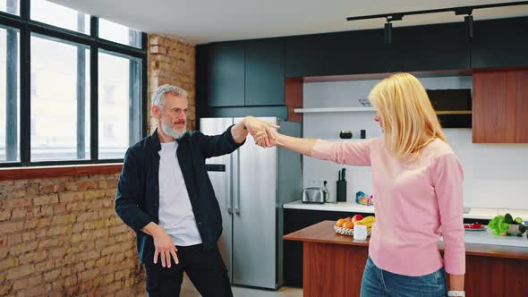 Mature Couple Graybearded Man and Beautiful Blonde Dancing in the Kitchen at Home alt