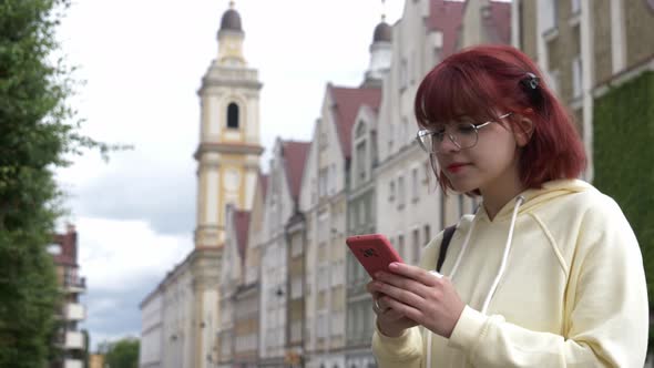 Young redhead Ukrainian teen girl with mobile phone on city street