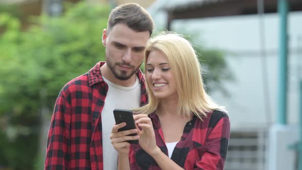 Young Happy Couple Using Phone Together in the Streets Outdoors