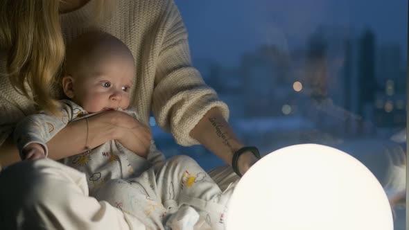 baby in mom's arms at night in the light of a ball lamp