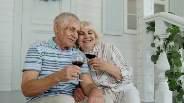 Attractive Senior Elderly Caucasian Couple Sitting and Drinking Wine in Porch at Home, Making a Kiss alt
