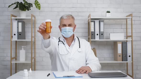 Doctor Wearing Face Mask Showing Pills Tube Advertising Medication Indoors alt