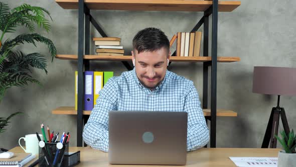 Smiling teacher man sitting on chair at desk in home open and start using laptop alt