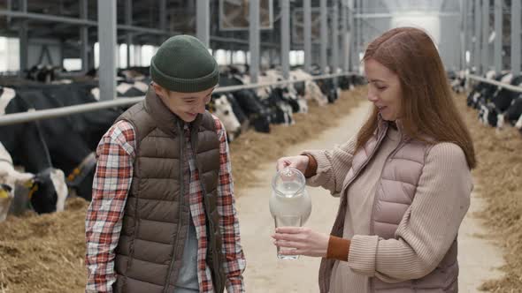 Woman Pouring Fresh Milk for Teenage Boy at Farm alt