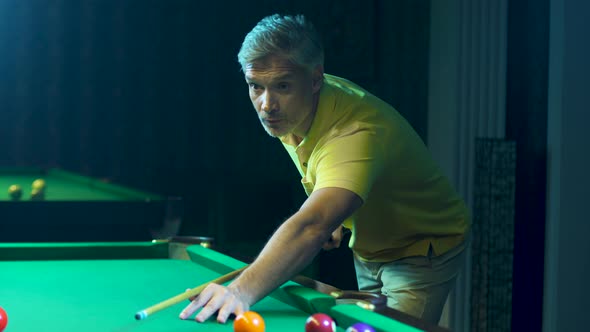 Man Holds a Cue, Takes Aim and Hits Billiard Ball. A Businessman Plays Snooker. alt