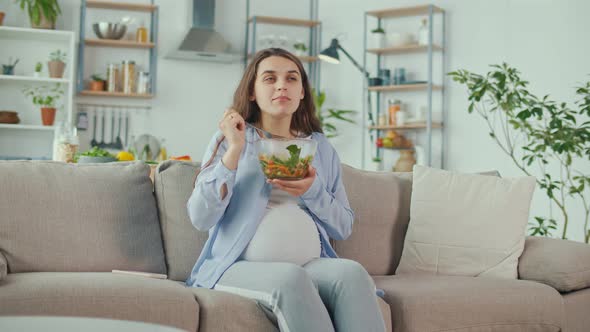 Pregnant Woman With Great Pleasure Eating Vegetable Salad on the Couch alt