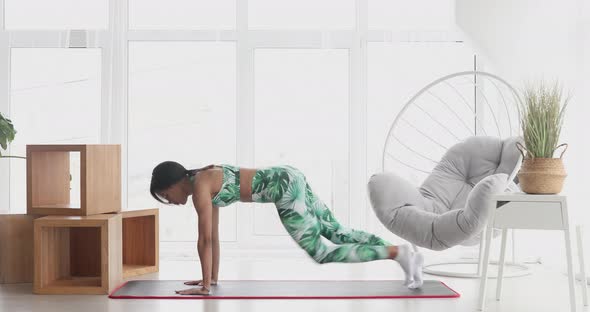 Young black woman making plank flexing legs exercise.