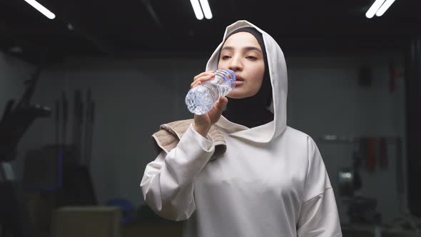 Young Muslim Fitness Woman Wearing a Sports Hijab Drinks Water After a Workout