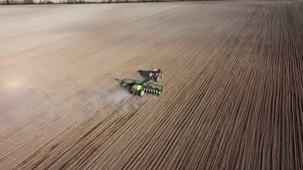 Aerial view of tractor with harrow system plowing ground on cultivated farmfield alt