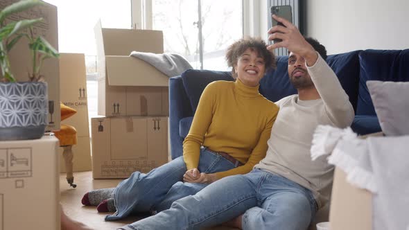 Couple In Lounge Taking Selfie On Mobile Phone With Unpacked Boxes In New Home On Moving Day