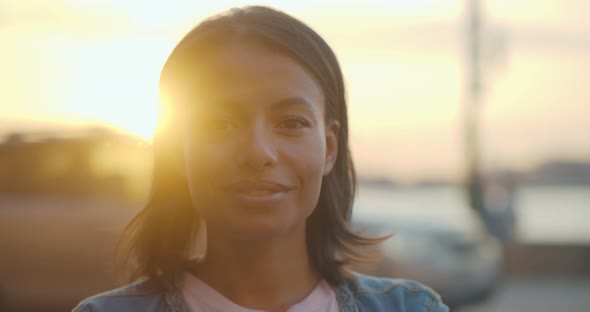 Bokeh Shot of Happy African Woman Looking at Camera Outdoors in Evening alt
