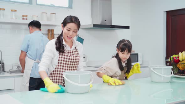 Asian happy young family teaching their daughter to clean kitchen counter in house with happiness. alt